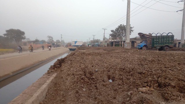 Before the plant: manure piled along the roadside canal at Gujjar Colony, with a livestock truck alongside