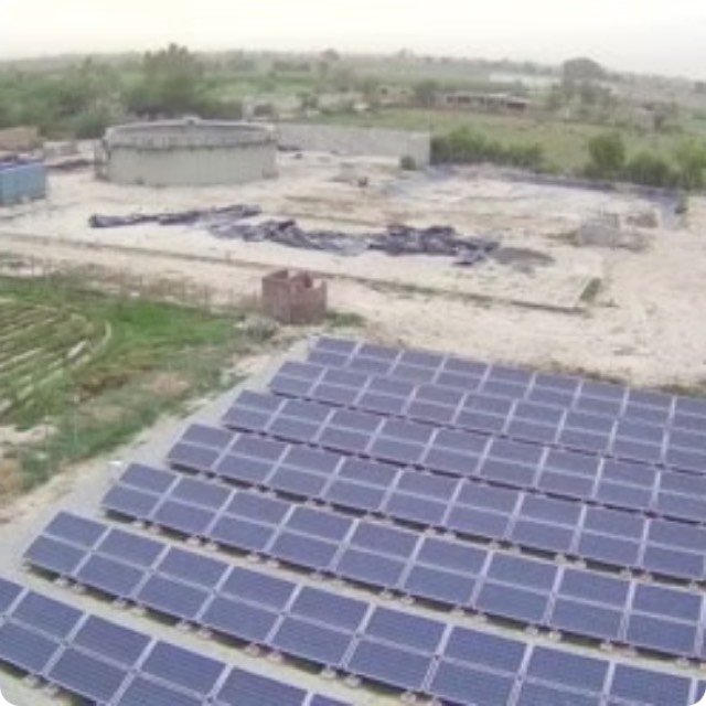 Solar array powering a community biogas plant, with the digester tank behind